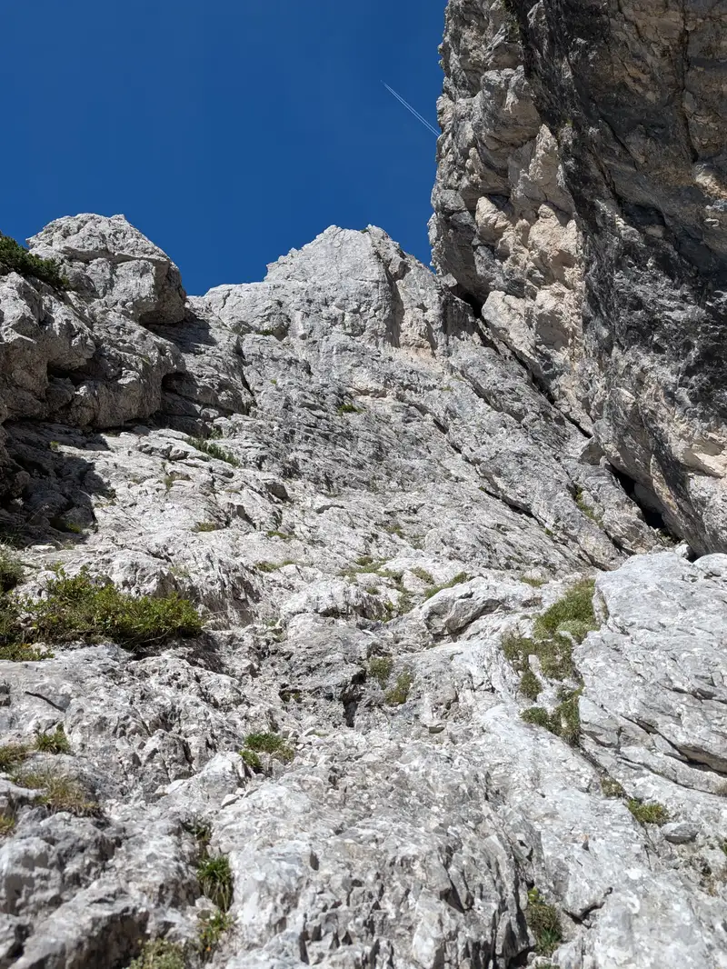 Terrain in the third pitch. According to the topo we should keep to the left and land under that lower shaded overhang. This is where fourth pitch starts. However we went more to the right side as far as yellow rocks, there is also a belay in there which we used as an anchor point and continued left via the ramp to tiny col under the rocky tower.